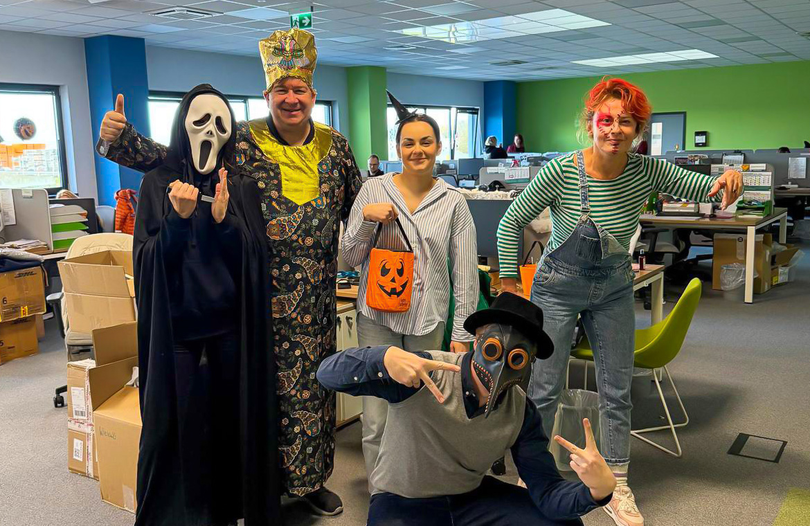 Pracownicy Lynka w strojach na Halloween pozują w biurze wśród dekoracji.